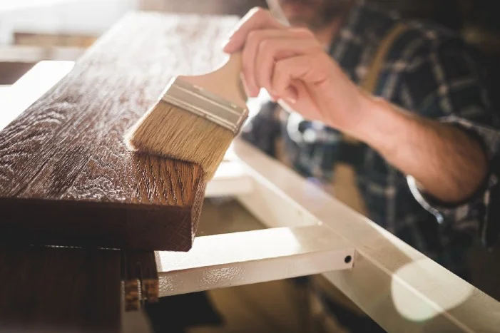 Person beizt Holz mit Pinsel